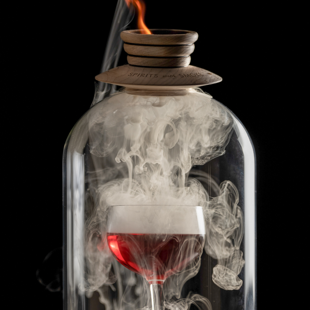 close up of a cocktail being smoked in a glass dome using spirits with smoke smoking saucer